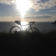 A bicycle on a grassy clifftop edge, silhouetted against an inky blue sea, white clouds and a lowering sun