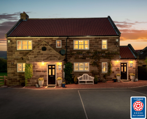 Exterior shot of a pretty brick cottage illuminated with interior and exterior lights against a setting sun